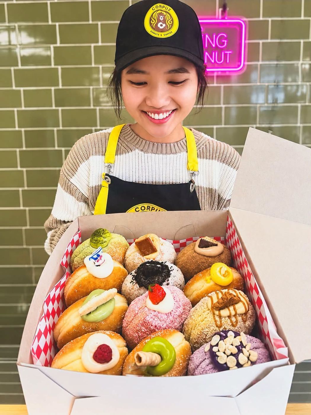 A Corpuz baker smiling with a full box of donuts